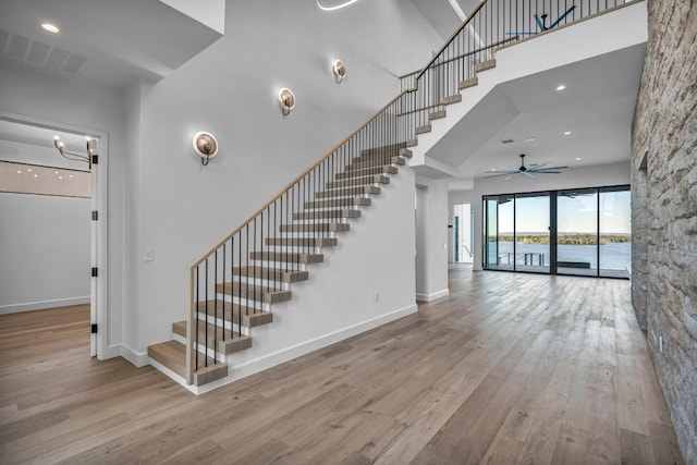 stairway featuring a high ceiling, a water view, hardwood / wood-style floors, and ceiling fan with notable chandelier