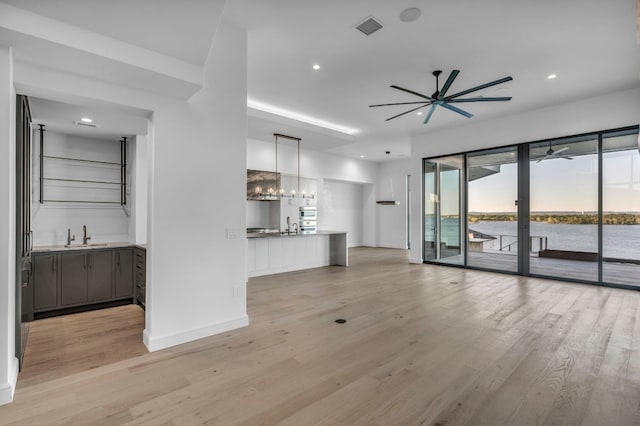 unfurnished living room featuring light hardwood / wood-style floors, ceiling fan with notable chandelier, sink, and a water view