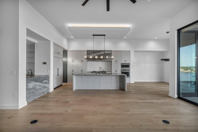 kitchen with a center island with sink, light hardwood / wood-style floors, sink, and double oven