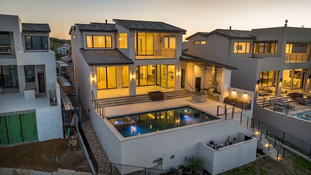 back house at dusk featuring a balcony, outdoor lounge area, and a patio area