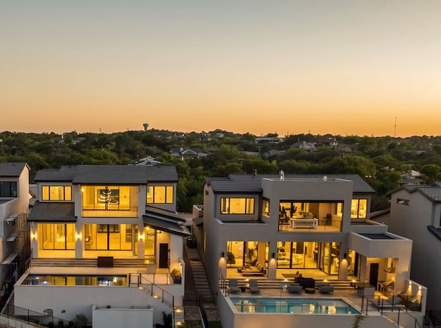 back house at dusk featuring an outdoor living space, a patio, and a balcony