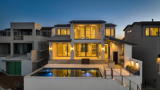 back house at dusk with a balcony and a patio area