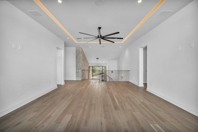 unfurnished living room with ceiling fan, a tray ceiling, and light hardwood / wood-style floors