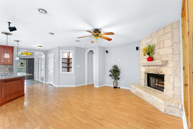 unfurnished living room featuring a stone fireplace, ceiling fan, and light hardwood / wood-style floors