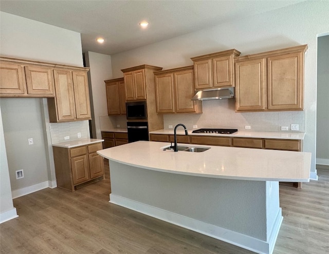 kitchen featuring stainless steel gas cooktop, built in microwave, sink, wood-type flooring, and a center island with sink