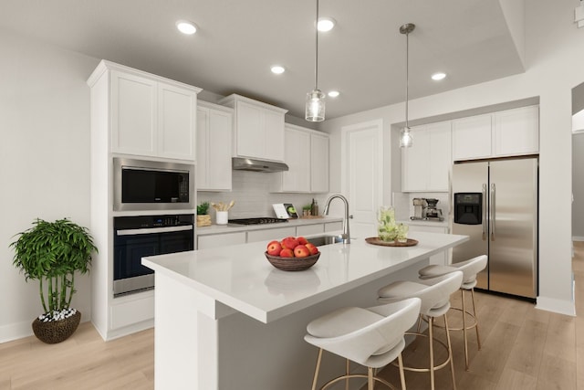 kitchen with appliances with stainless steel finishes, a kitchen island with sink, sink, white cabinets, and light hardwood / wood-style floors