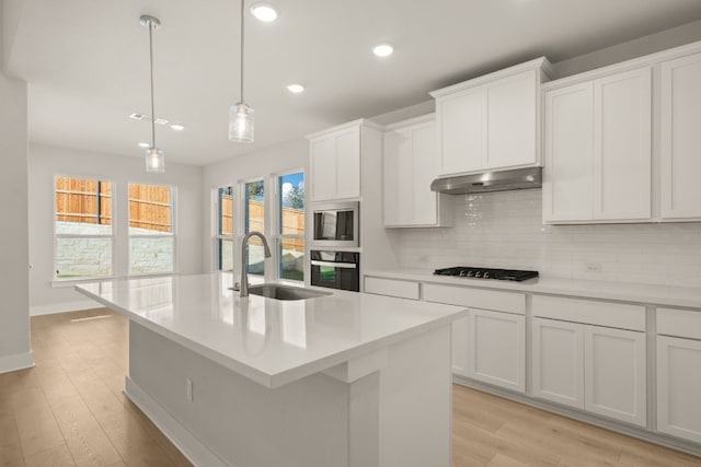 kitchen featuring light wood-type flooring, stainless steel appliances, a center island with sink, and sink