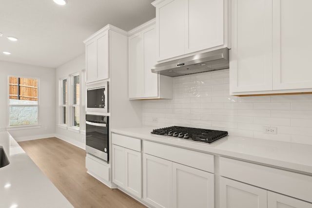 kitchen featuring stainless steel appliances, backsplash, light hardwood / wood-style floors, white cabinets, and exhaust hood