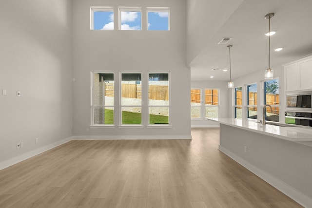 unfurnished living room with a towering ceiling, light wood-type flooring, and sink