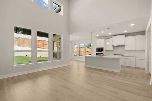 kitchen featuring a kitchen island with sink, white cabinets, hanging light fixtures, light wood-type flooring, and stovetop