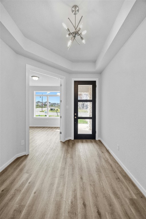 entryway featuring light wood-type flooring, a tray ceiling, and a chandelier