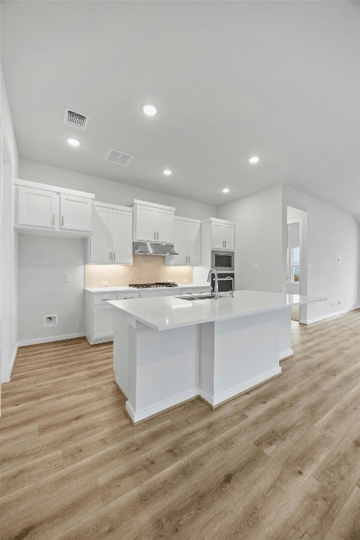 kitchen featuring stainless steel microwave, sink, light hardwood / wood-style floors, a center island with sink, and white cabinets