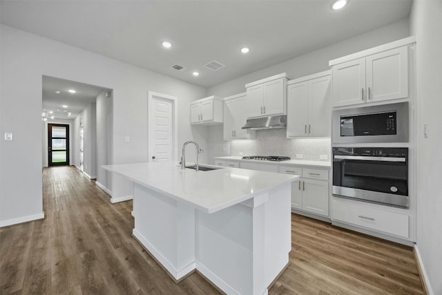 kitchen featuring hardwood / wood-style floors, sink, an island with sink, appliances with stainless steel finishes, and white cabinetry