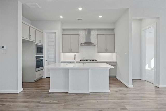 kitchen featuring sink, an island with sink, stainless steel appliances, and wall chimney range hood