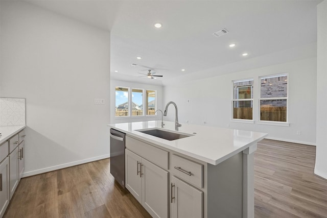 kitchen featuring ceiling fan, sink, light hardwood / wood-style flooring, stainless steel dishwasher, and a center island with sink