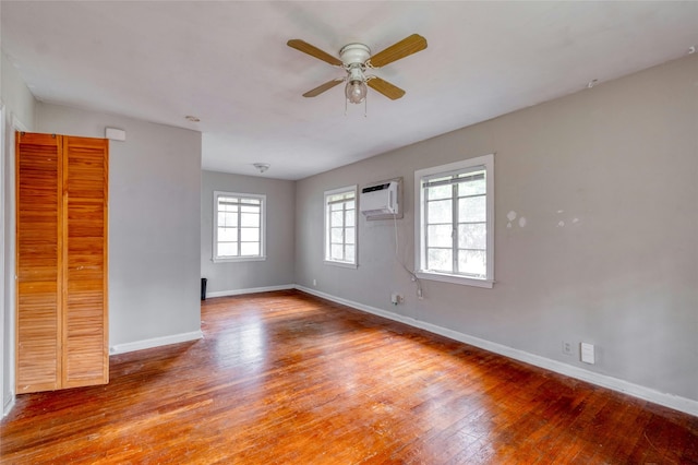 spare room featuring hardwood / wood-style floors, a wealth of natural light, an AC wall unit, and ceiling fan