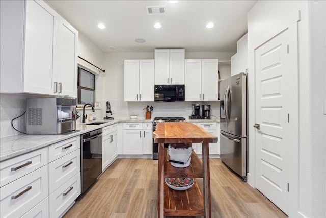 kitchen with light hardwood / wood-style flooring, backsplash, white cabinetry, black appliances, and sink