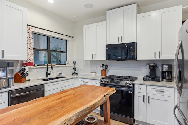 kitchen with light hardwood / wood-style floors, tasteful backsplash, black appliances, white cabinets, and sink