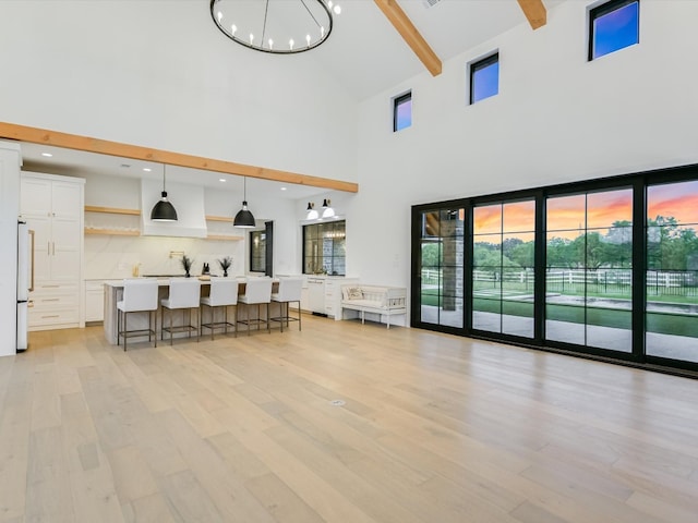 living room with high vaulted ceiling, beamed ceiling, an inviting chandelier, and light hardwood / wood-style flooring