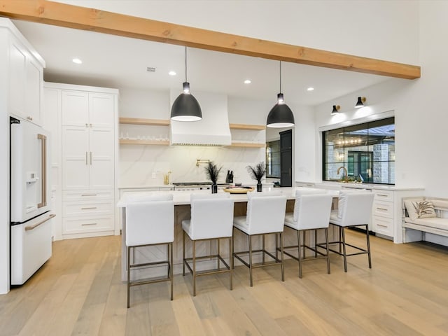 kitchen with backsplash, white cabinetry, high end white refrigerator, and a kitchen island with sink