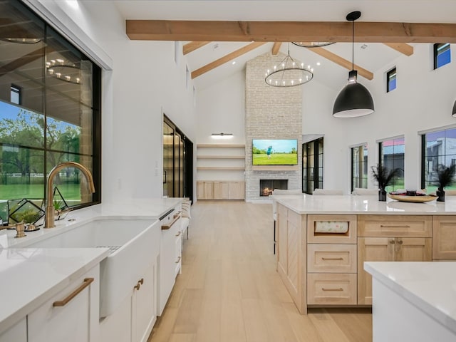 kitchen featuring beam ceiling, a fireplace, light wood-type flooring, light brown cabinetry, and a notable chandelier