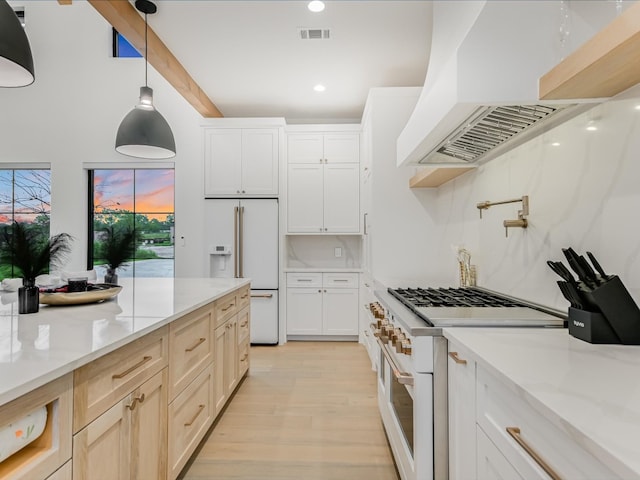 kitchen with light wood-type flooring, premium range hood, light stone counters, decorative light fixtures, and high end appliances