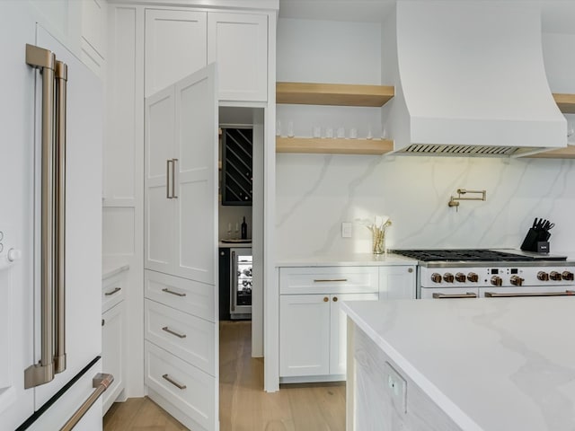 kitchen with wine cooler, light hardwood / wood-style flooring, tasteful backsplash, premium range hood, and white cabinetry