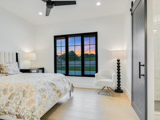 bedroom featuring a water view, ceiling fan, a barn door, and light hardwood / wood-style flooring