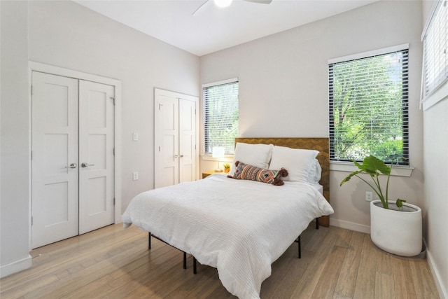 bedroom featuring ceiling fan, light wood-type flooring, and multiple closets