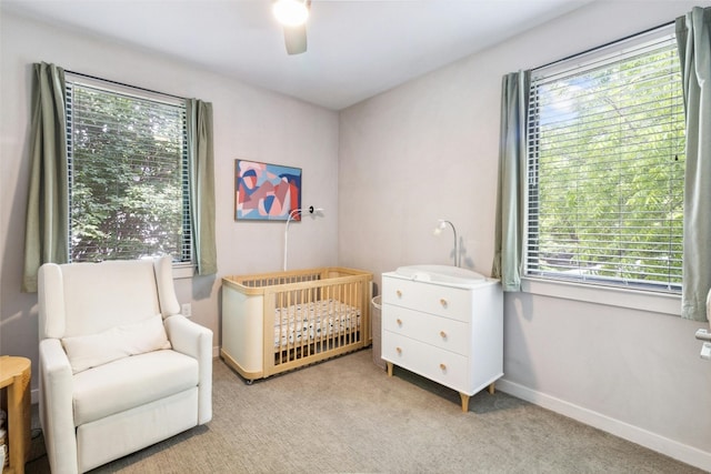 carpeted bedroom with a crib, multiple windows, and ceiling fan