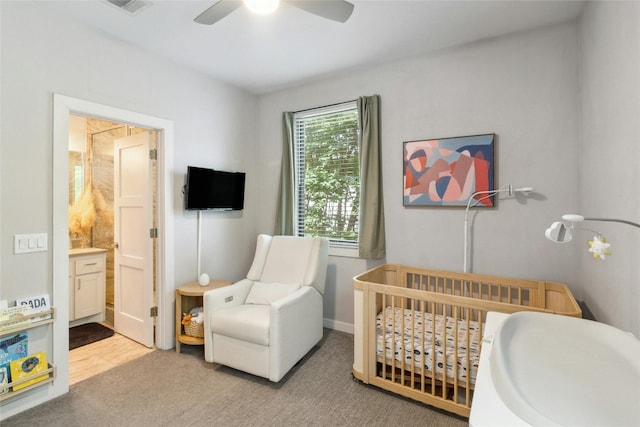 bedroom with a nursery area, light hardwood / wood-style floors, ensuite bathroom, and ceiling fan