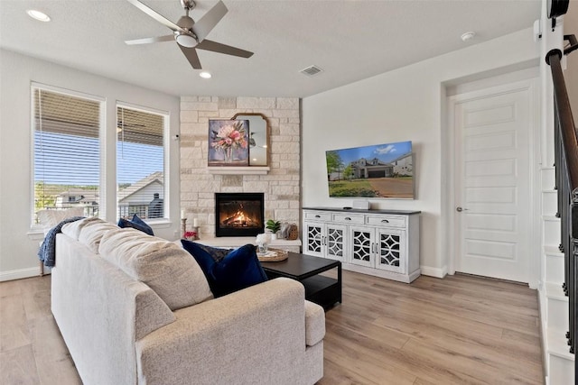 living room featuring a stone fireplace, light hardwood / wood-style floors, ceiling fan, and a textured ceiling