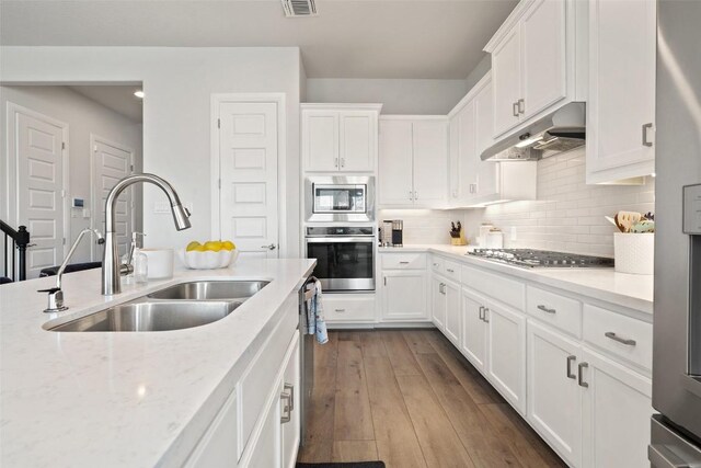 kitchen with dark wood-type flooring, sink, light stone countertops, white cabinets, and appliances with stainless steel finishes