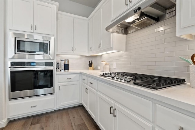 kitchen featuring appliances with stainless steel finishes, white cabinetry, backsplash, dark hardwood / wood-style floors, and ventilation hood