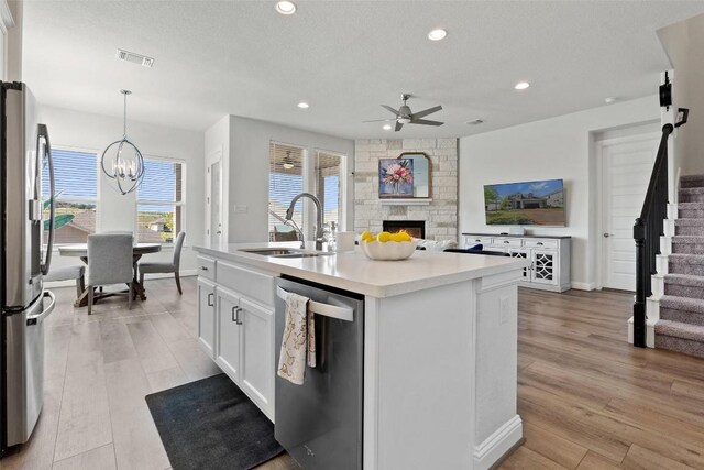 kitchen with sink, white cabinetry, stainless steel appliances, a center island with sink, and decorative light fixtures