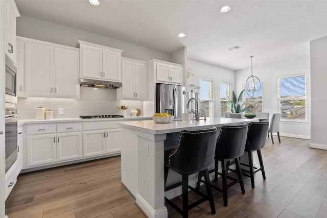 kitchen with a kitchen island with sink, pendant lighting, white cabinets, and appliances with stainless steel finishes