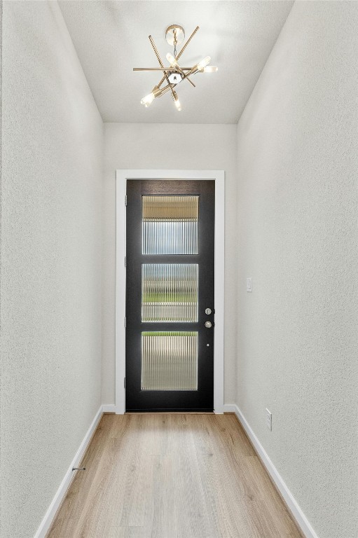 doorway to outside with a notable chandelier and light wood-type flooring