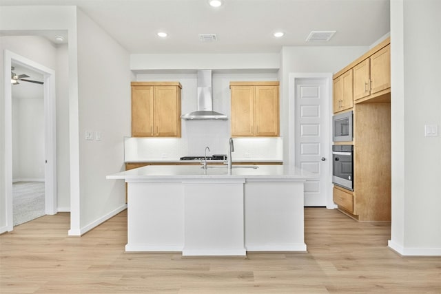 kitchen featuring backsplash, light hardwood / wood-style flooring, wall chimney exhaust hood, an island with sink, and appliances with stainless steel finishes