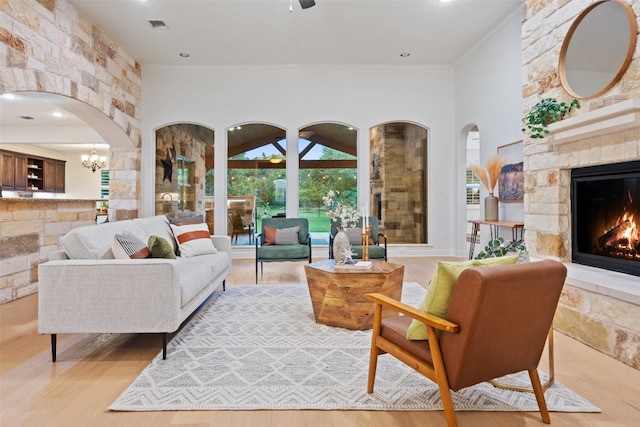 living room with hardwood / wood-style floors, a stone fireplace, crown molding, and an inviting chandelier