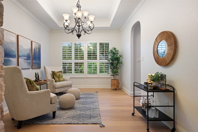 living area featuring a raised ceiling, light hardwood / wood-style flooring, ornamental molding, and a notable chandelier