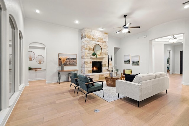 living room featuring ceiling fan, a stone fireplace, light wood-type flooring, and crown molding