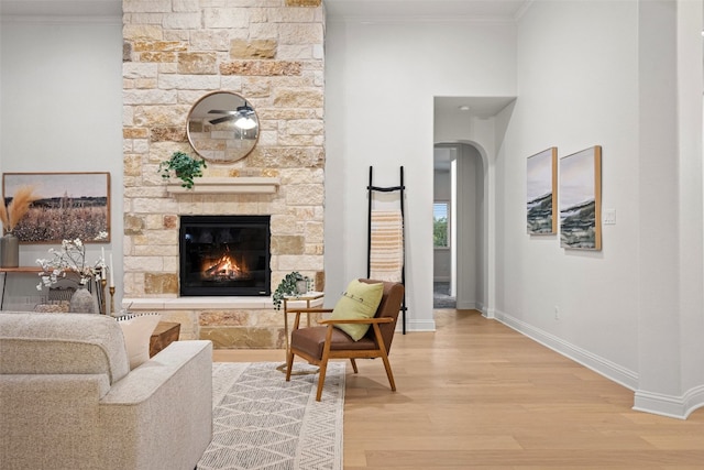 living room with wood-type flooring, a stone fireplace, and crown molding