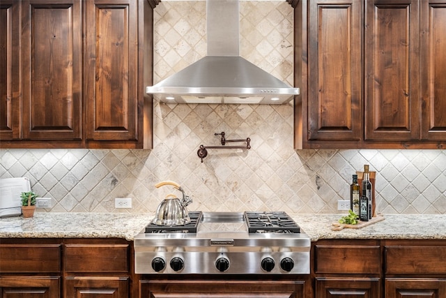 kitchen featuring decorative backsplash, wall chimney exhaust hood, light stone counters, and stainless steel gas cooktop