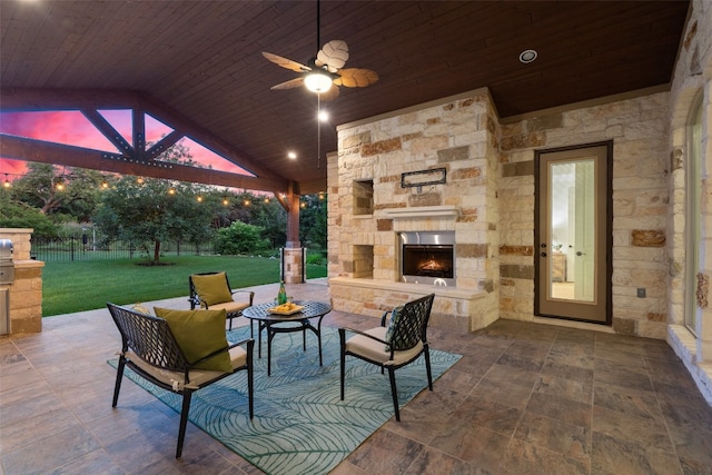 patio terrace at dusk featuring a lawn, ceiling fan, and an outdoor living space with a fireplace