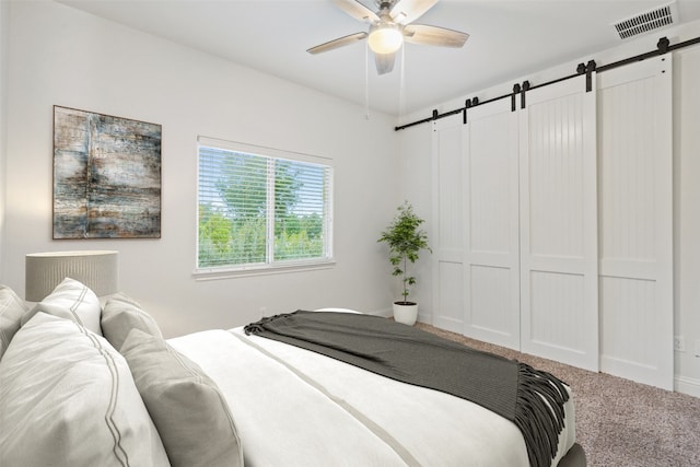 bedroom with ceiling fan, a barn door, carpet floors, and a closet