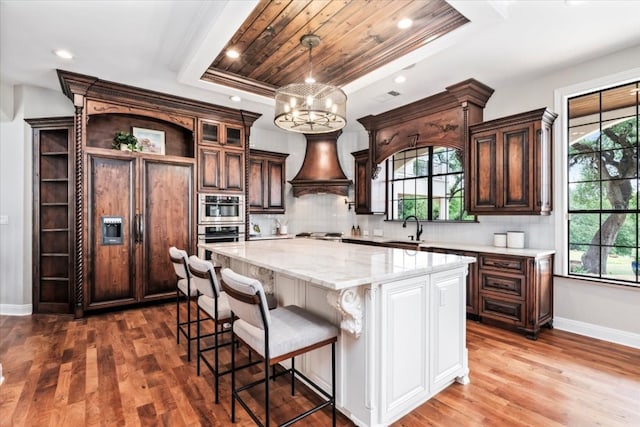 kitchen with a tray ceiling, premium range hood, a center island, paneled built in refrigerator, and hardwood / wood-style flooring