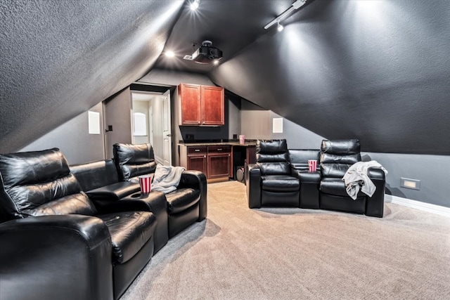 carpeted home theater featuring vaulted ceiling and rail lighting