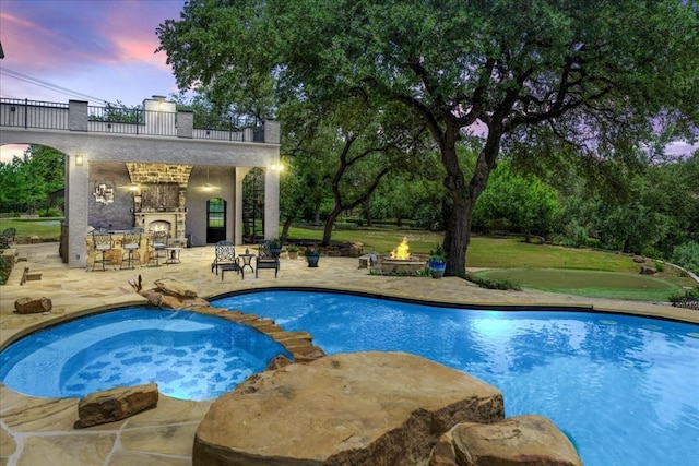 pool at dusk with an in ground hot tub, a patio area, and a lawn