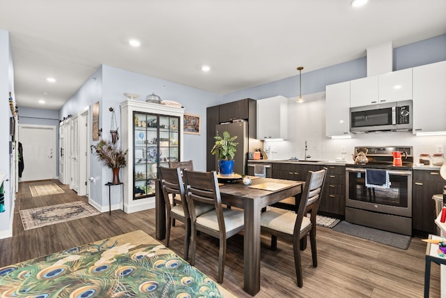 kitchen with decorative light fixtures, backsplash, hardwood / wood-style floors, dark brown cabinets, and appliances with stainless steel finishes