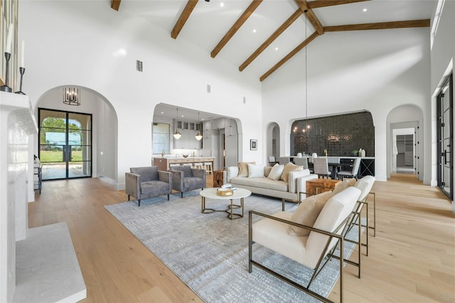 living area featuring light wood-style flooring, a chandelier, arched walkways, and beamed ceiling